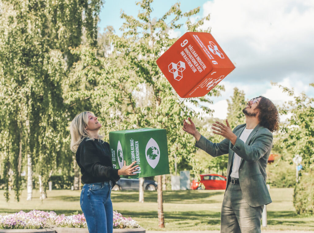 Två människor kastar kuddar med hållbarhetsmålen till varandra.